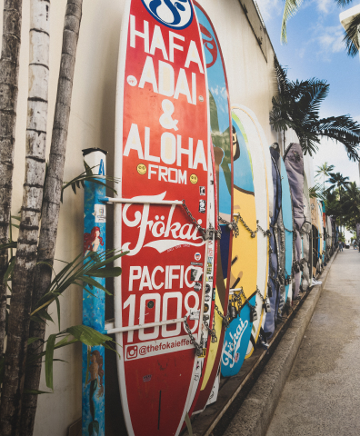A series of colorful surfboards in a rack along a sidewalk in O’ahu, Hawai'i.
